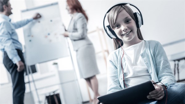 ילדה עם אוזניות צופה בטבלט ברקע אנשים עובדים במשרד